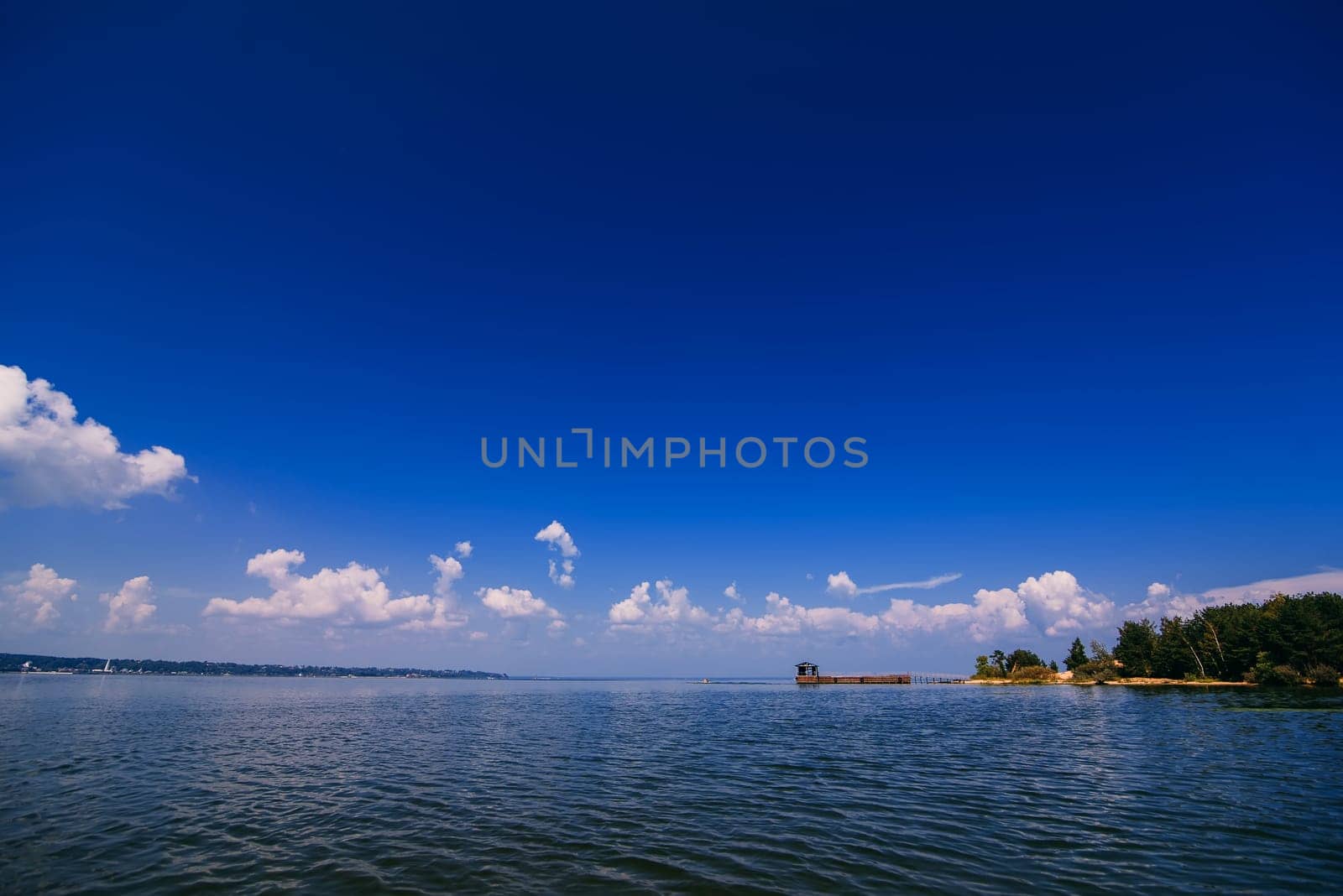blue sky over the water of the river with a jetty and a sandy beach on a summer day
