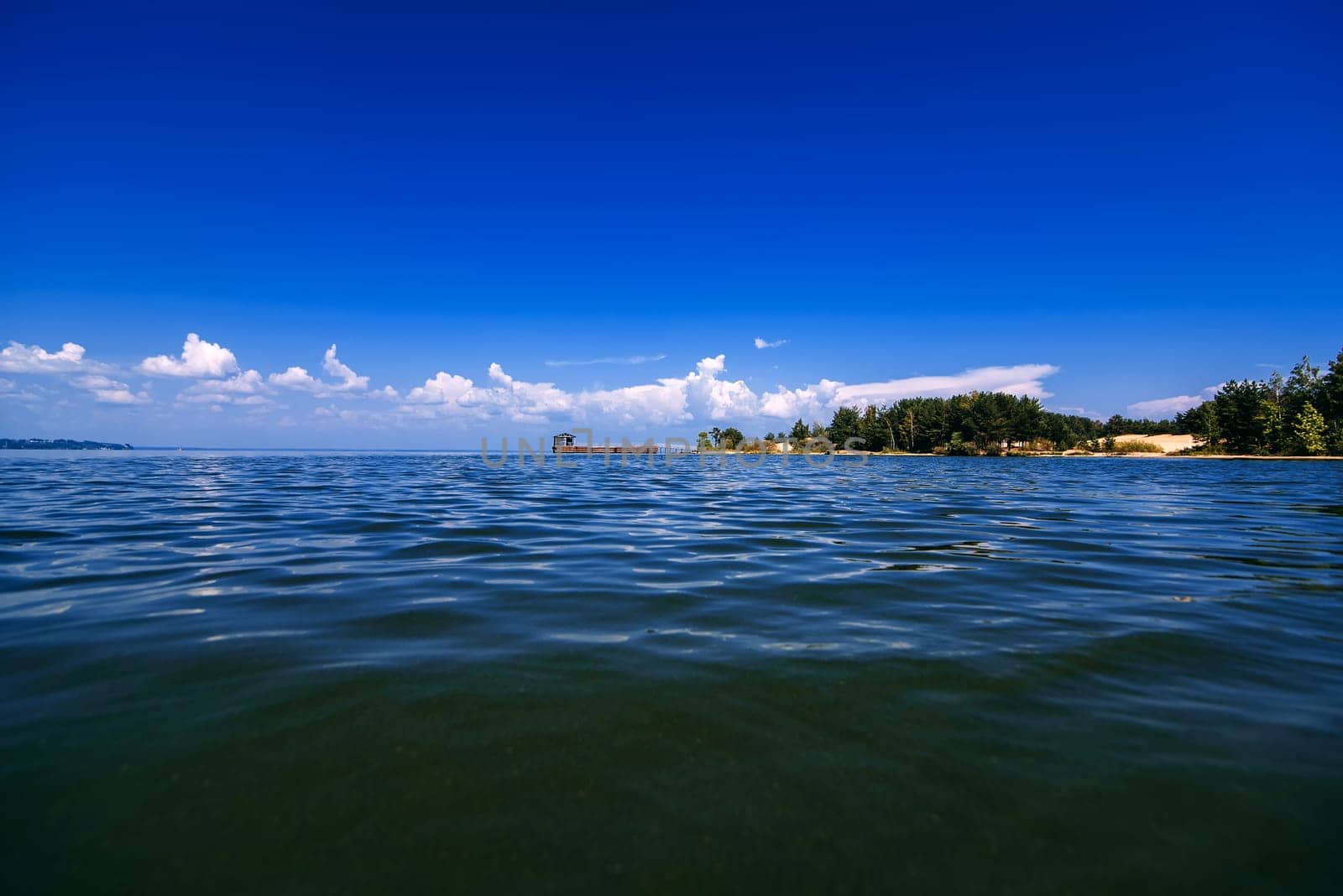 blue sky with white clouds over the water on a summer day with a jetty and shore in the distance