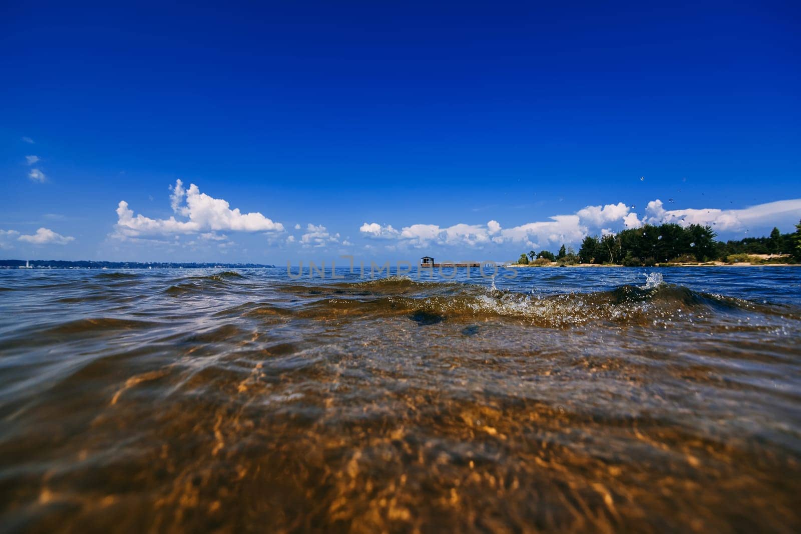blue clear sky with white clouds over the water on a summer day and a beach with waves