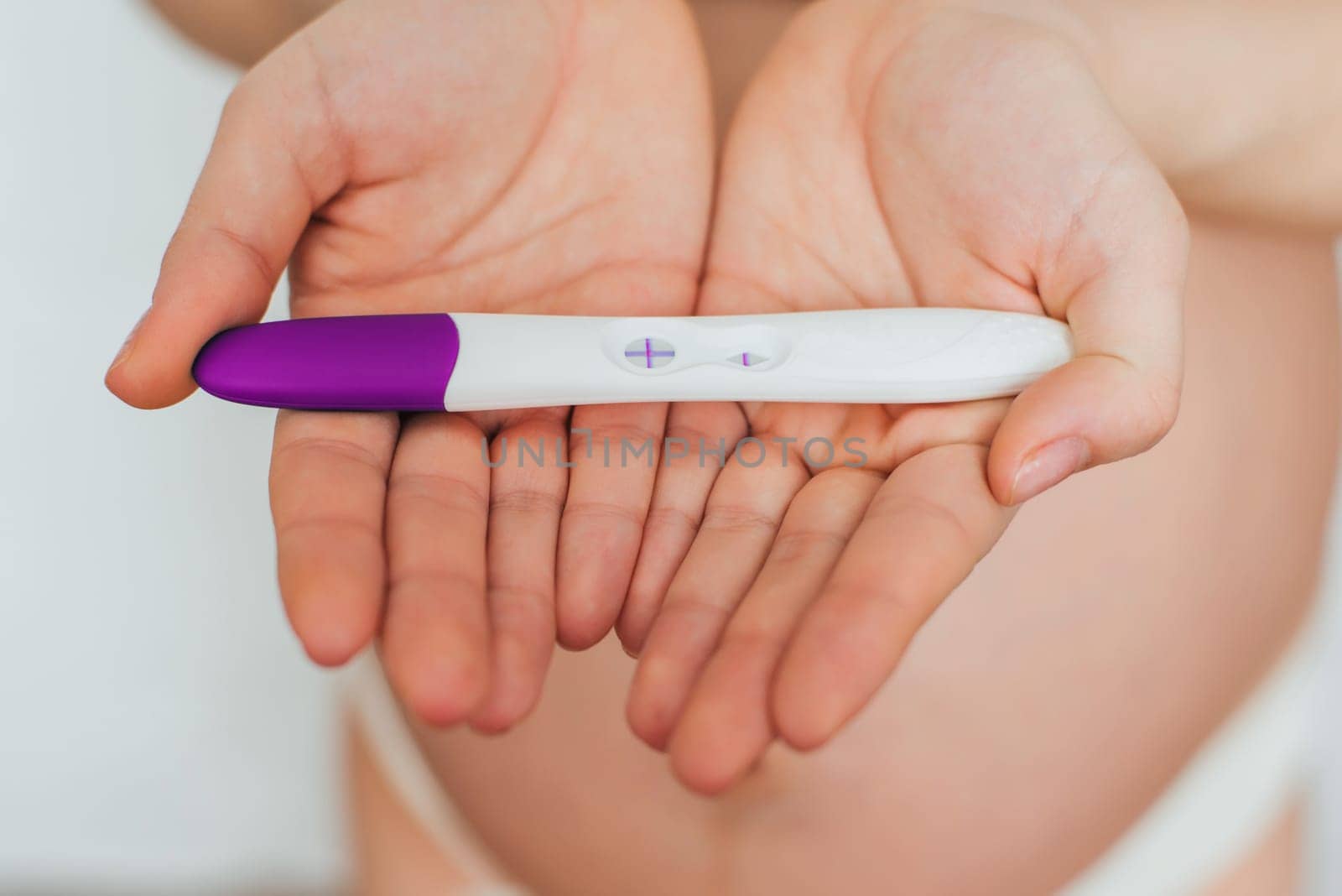 positive pregnancy test in the hands of a pregnant girl on the background of the abdomen