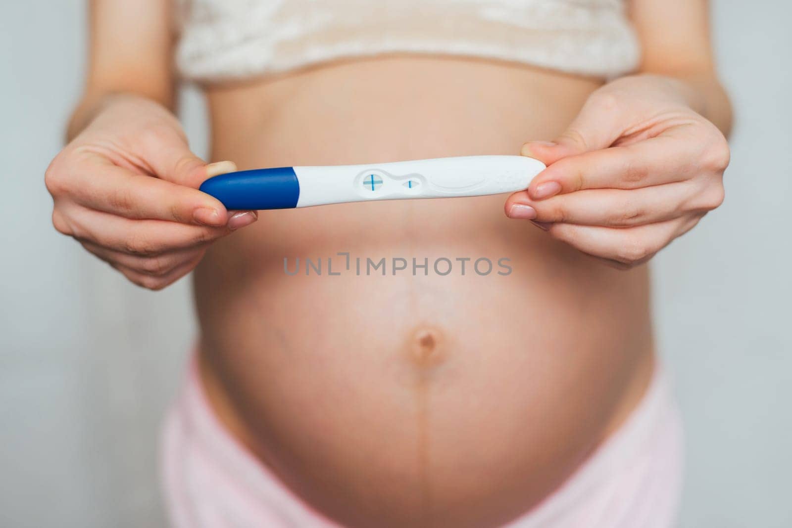positive pregnancy test in the hands of a pregnant girl on the background of the abdomen