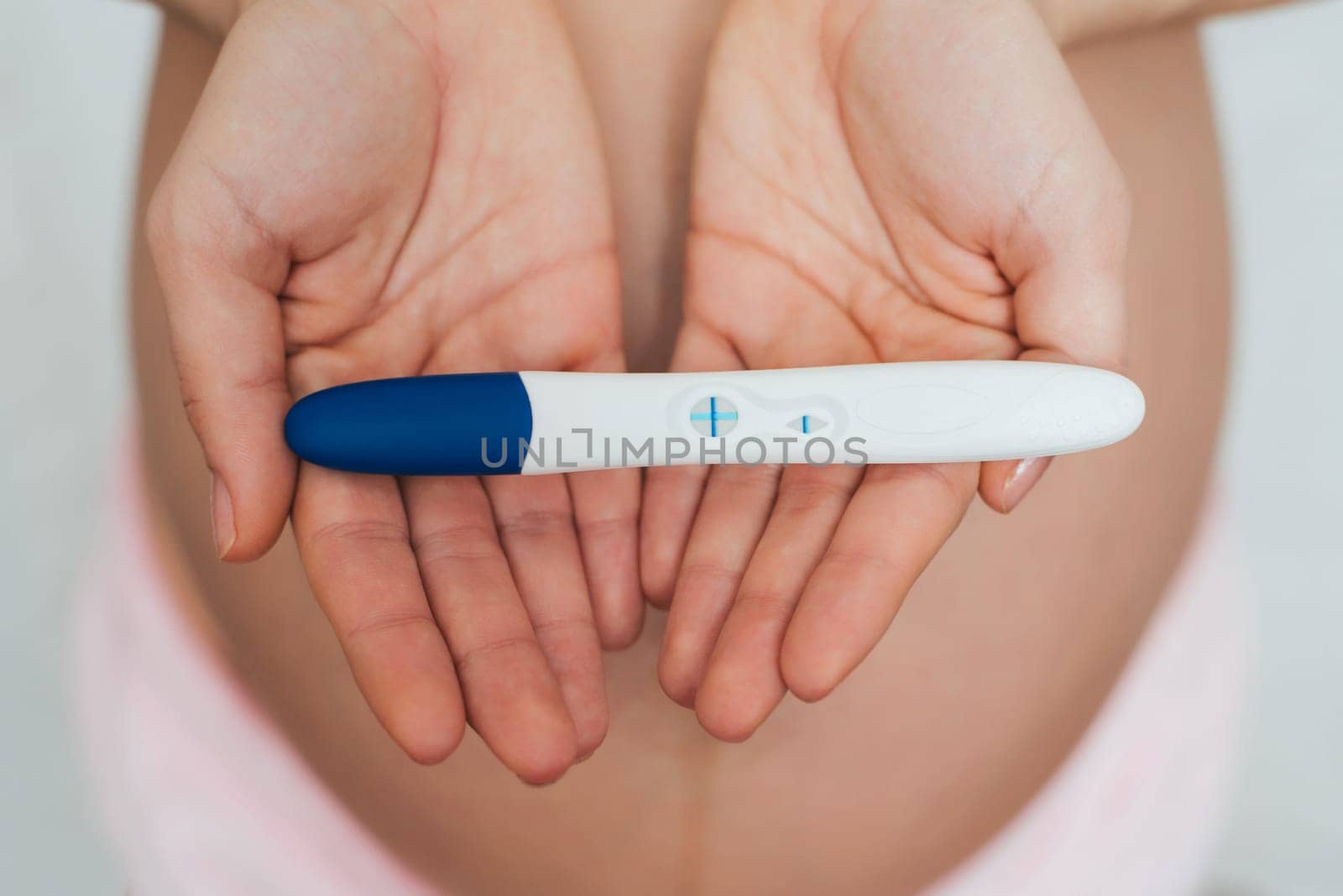positive pregnancy test in the hands of a pregnant girl on the background of the abdomen