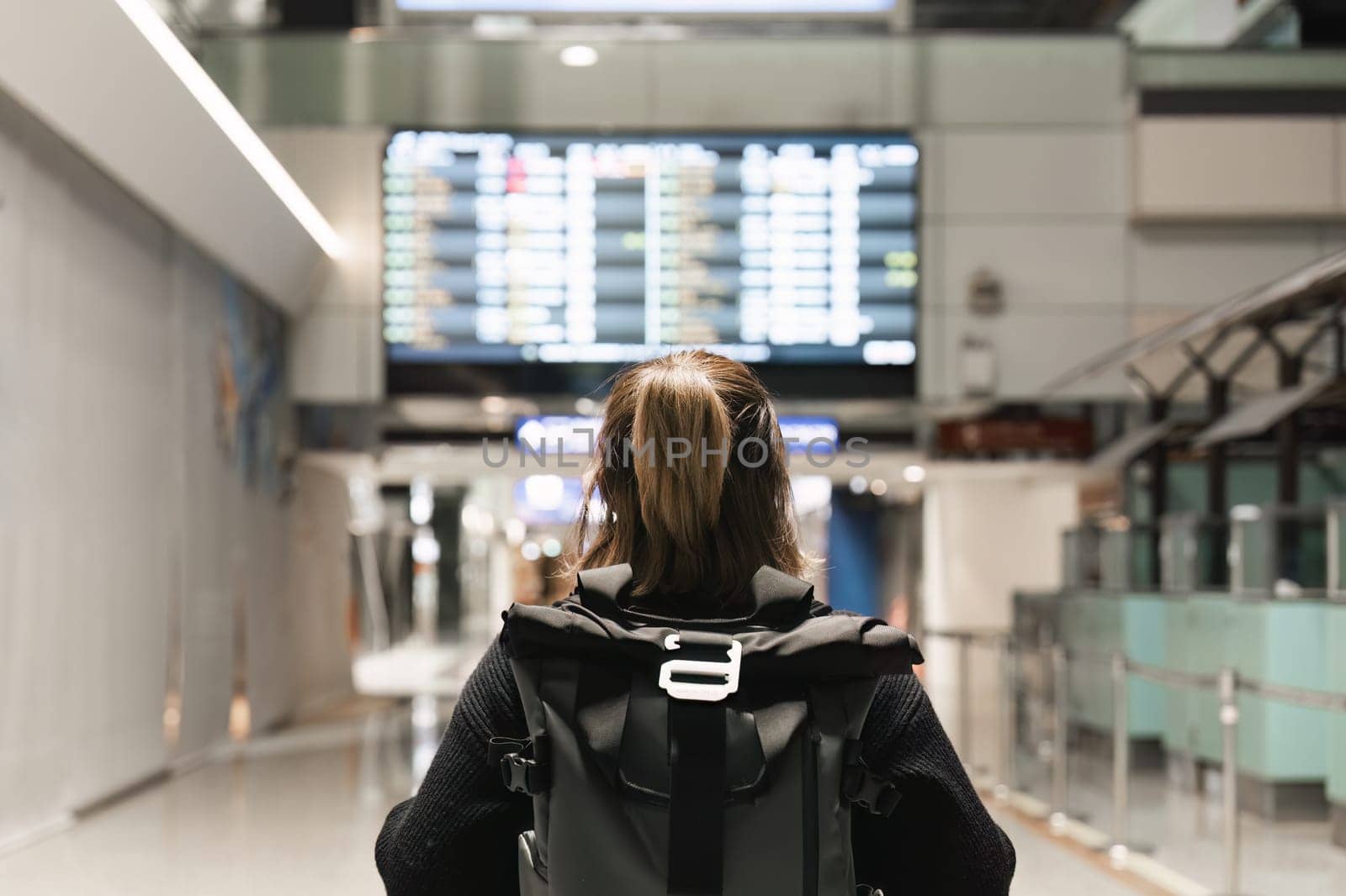 Young woman backpack in international airport terminal looking at the flight schedule information board, checking her flight.