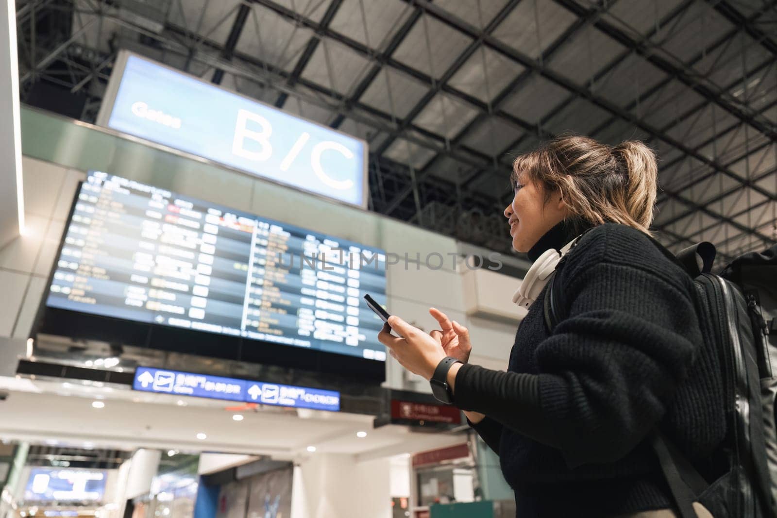 Woman in international airport, using mobile smartphone and checking flight schedule at the flight information board by nateemee