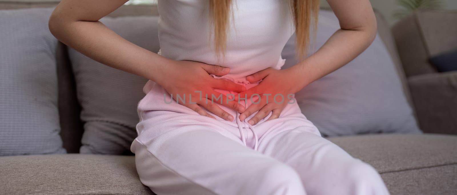 Young woman suffering from stomach ache on sofa at home.