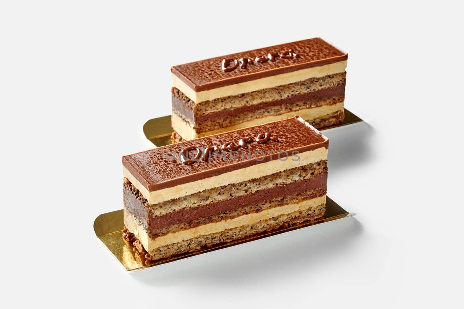 Cake slices with layers of walnut sponge pastry soaked in coffee syrup, chocolate ganache and buttercream, with word Opera written on chocolate glaze, isolated on white. French style confectionery