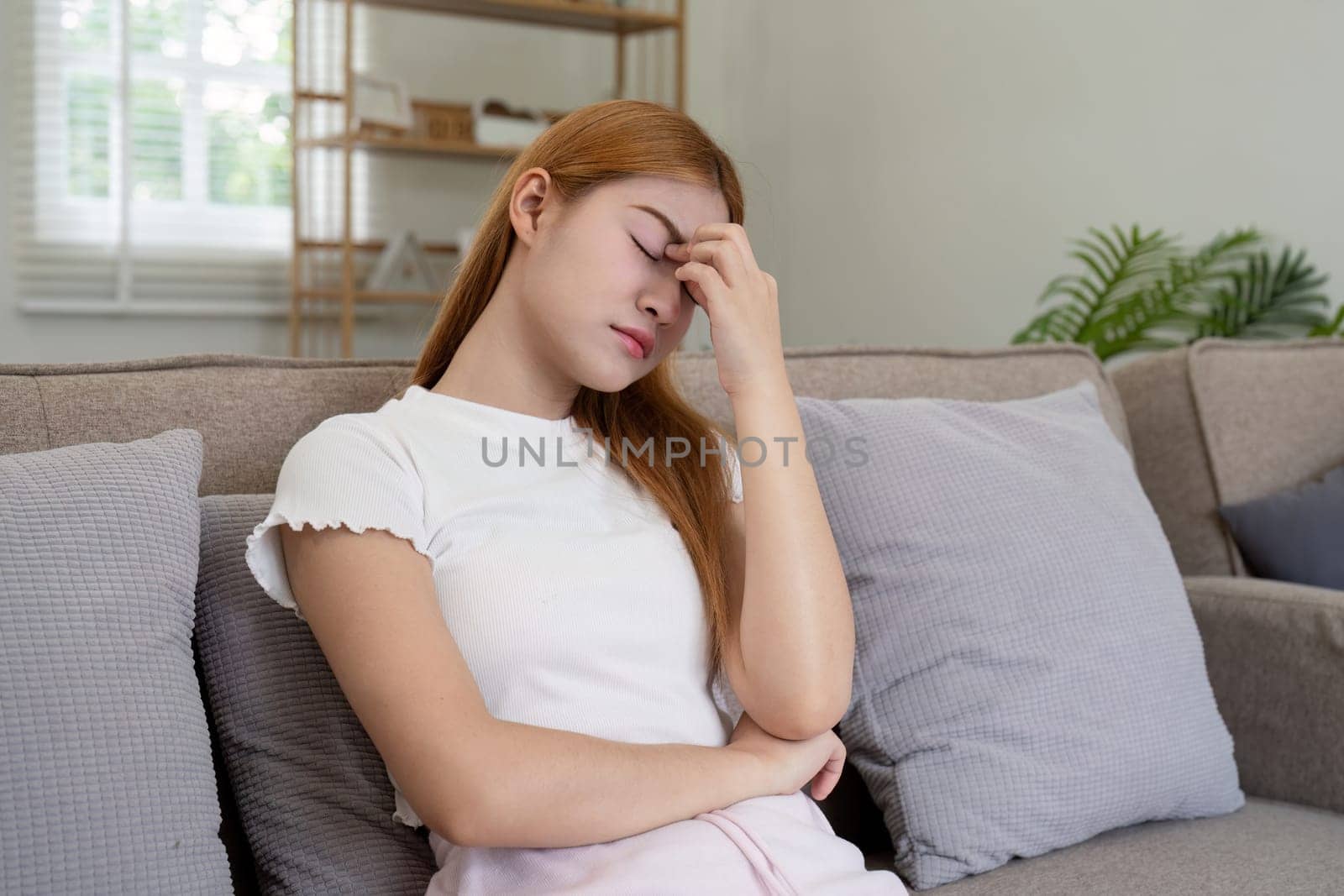 Woman asian frustrated ill sit sofa suffer headache migraine pain have health problem in house living room.