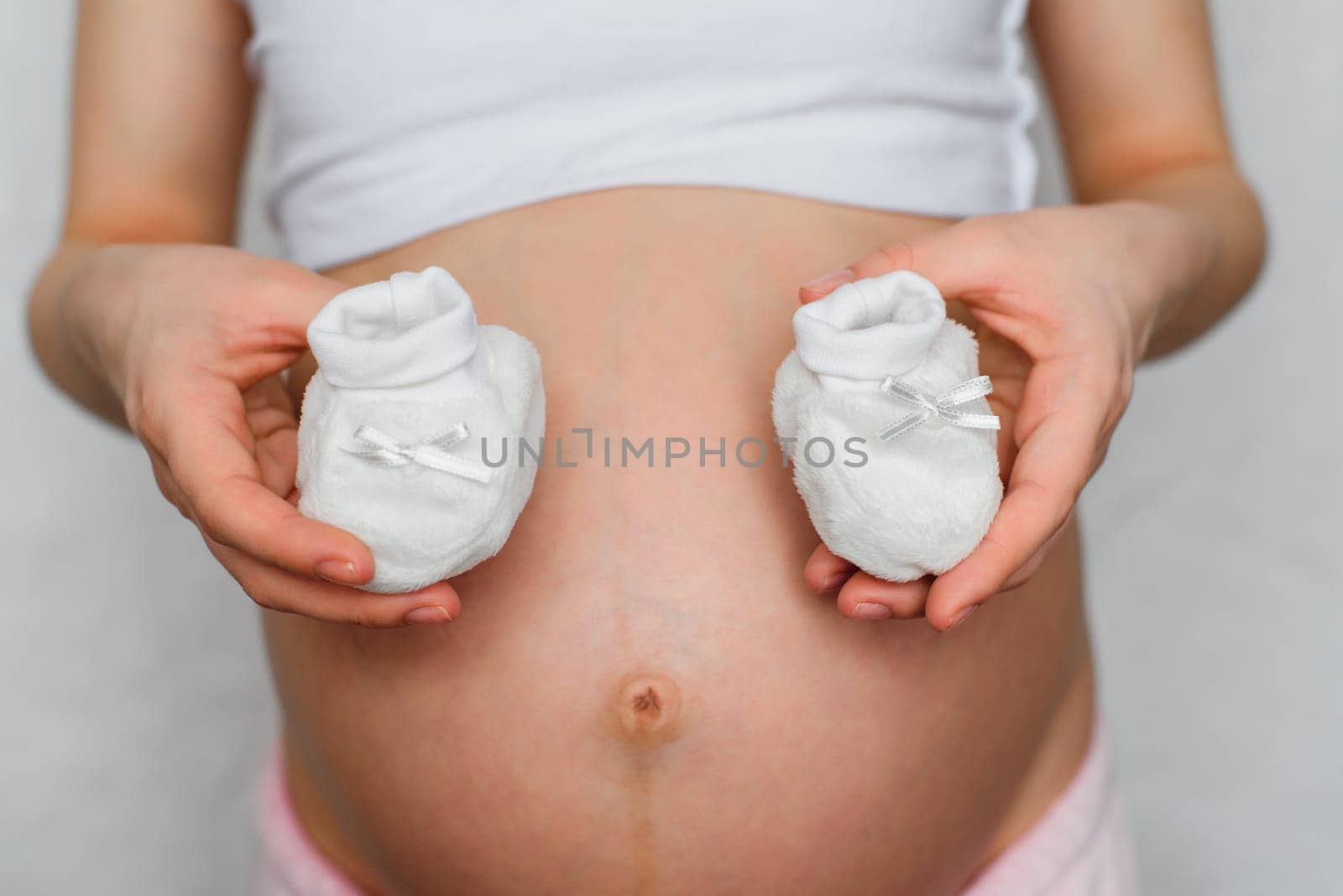 booties for newborn in the hands of a pregnant girl on the background of the abdomen waiting for the baby