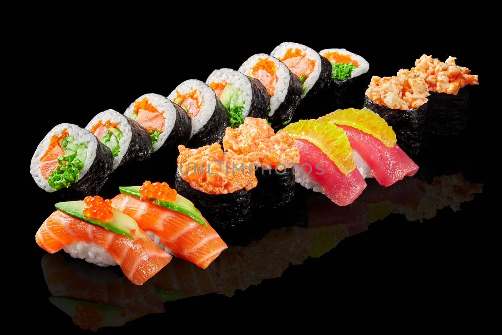Enticing vibrant set of futomaki, gunkan maki and nigiri sushi with salmon and tuna garnished with caviar, cucumber and orange pulp, presented on reflective black surface. Japanese fusion cuisine