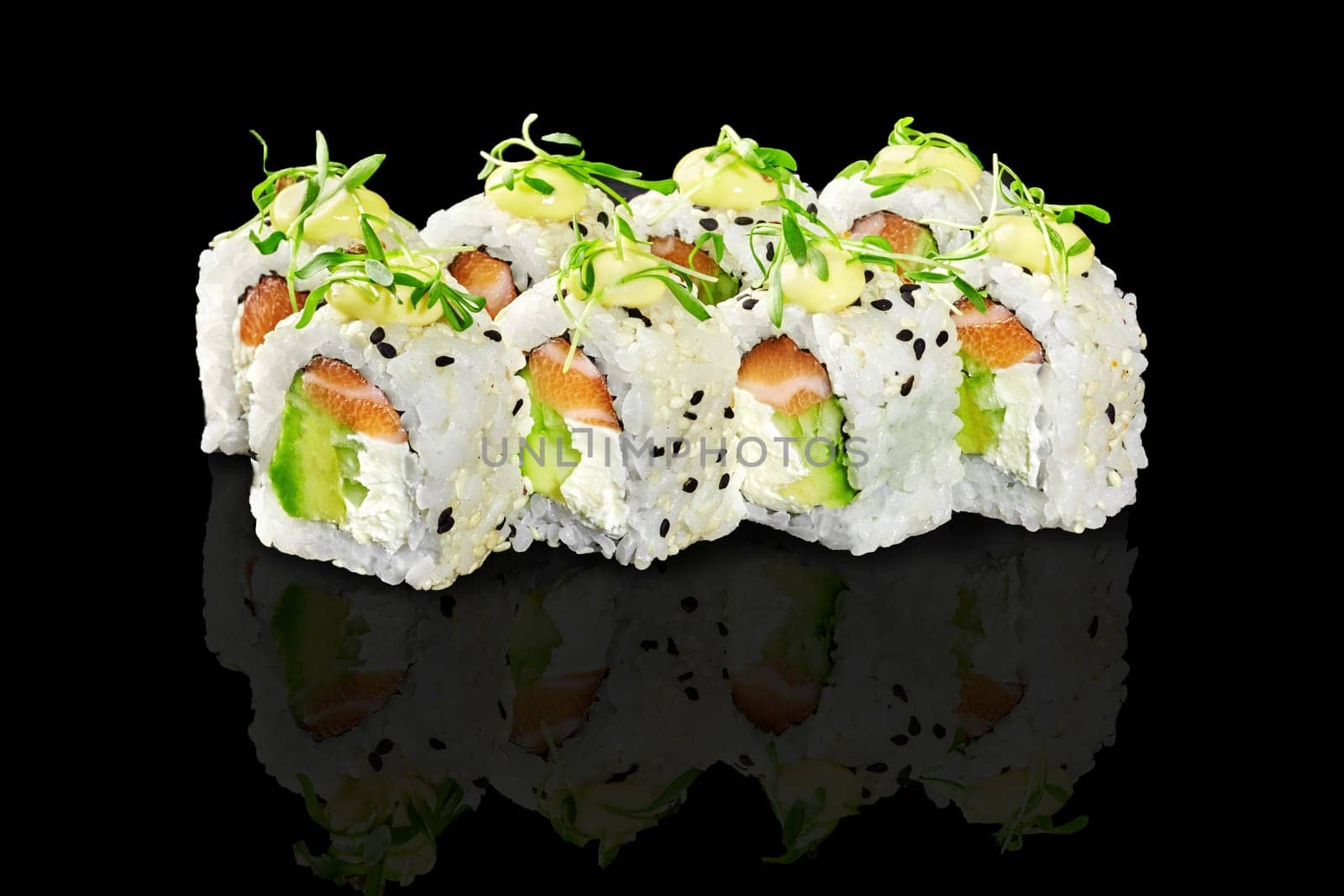 Sesame coated sushi rolls with cream cheese, avocado and fresh salmon, garnished with microgreens and drizzle of mayo, presented on reflective black surface. Japanese cuisine