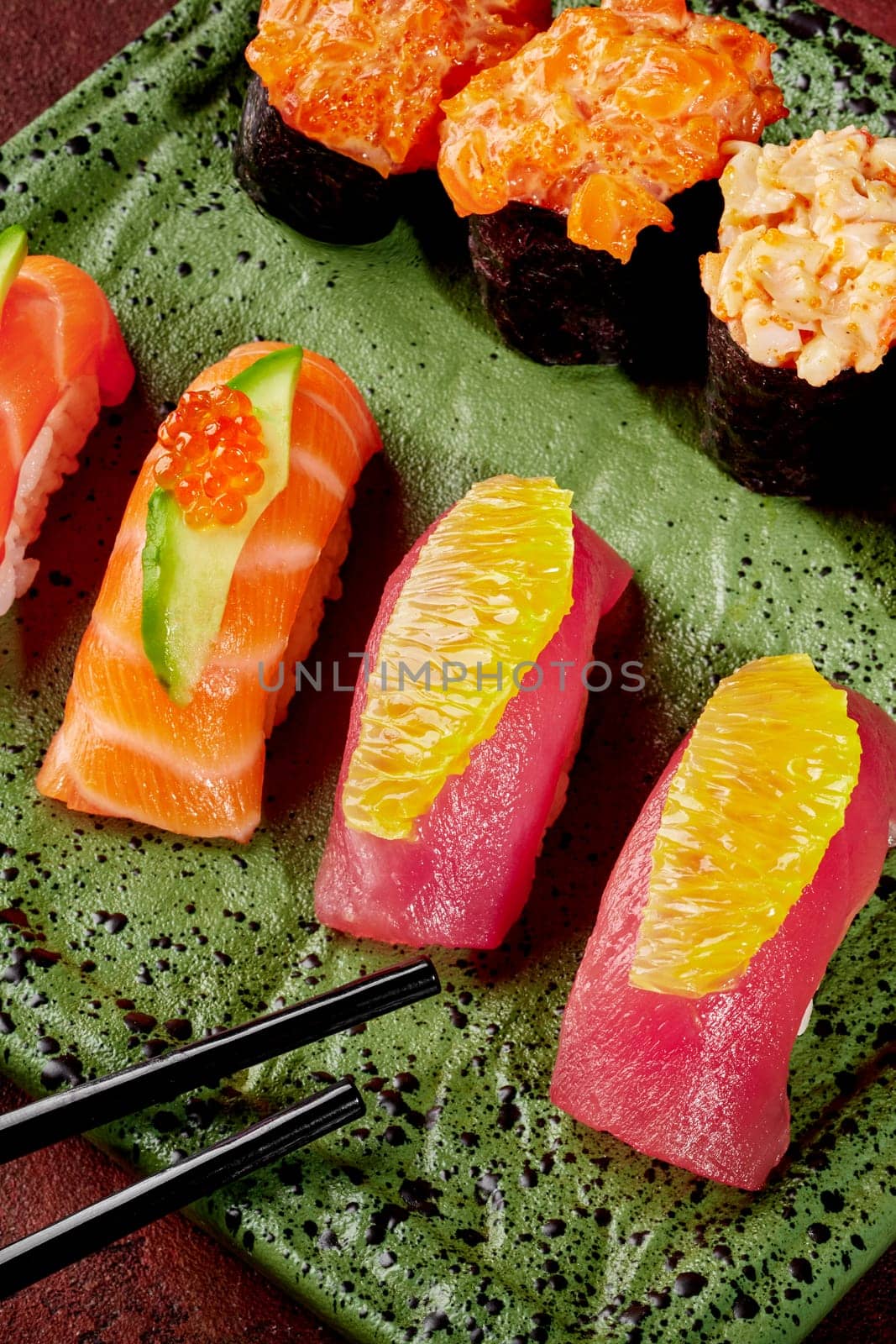 Delectable nigiri sushi with slices of fresh tuna and salmon, adorned with orange, cucumber, and caviar, served on speckled green plate with gunkan maki and chopsticks ready for Japanese style lunch