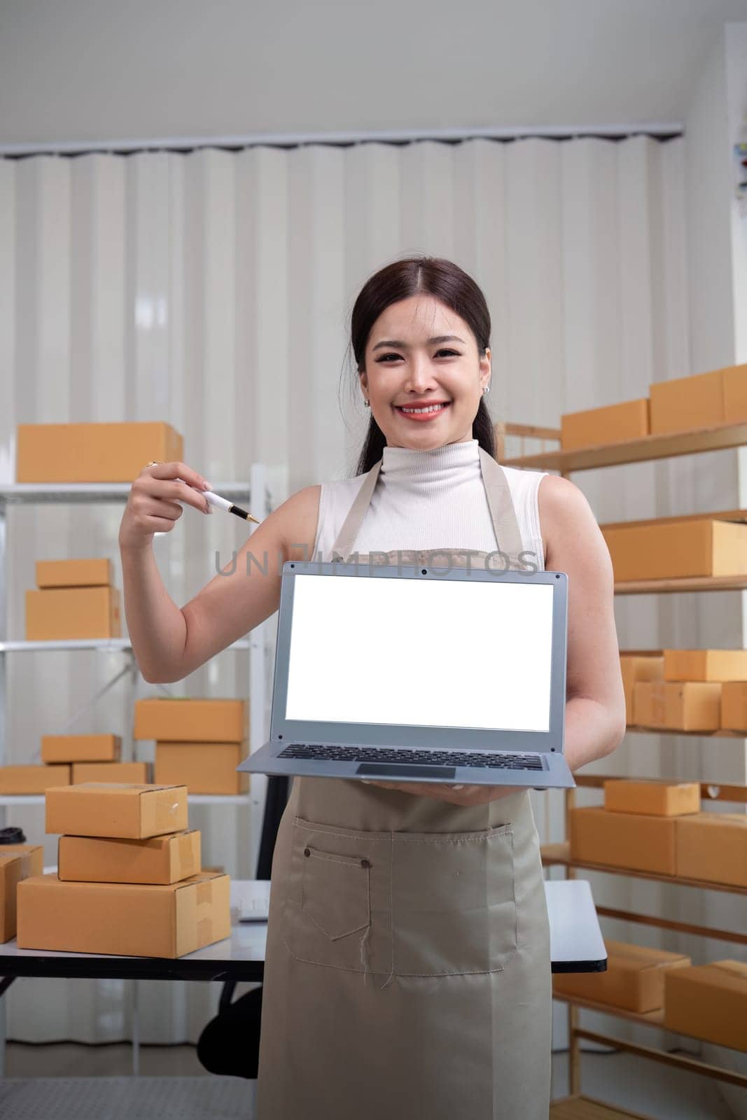 Young business woman asian working online ecommerce shopping at her shop. Young woman sell prepare parcel box of product for deliver to customer. Online selling and mockup using laptop by nateemee
