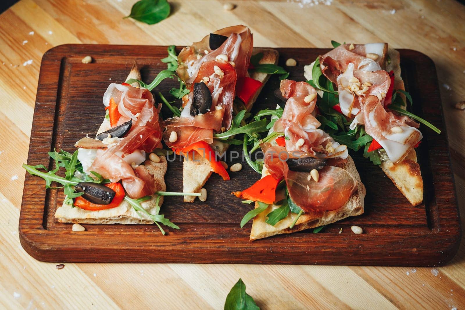 Four delectable bruschetta topped with prosciutto and olives displayed on a rustic wooden cutting board.