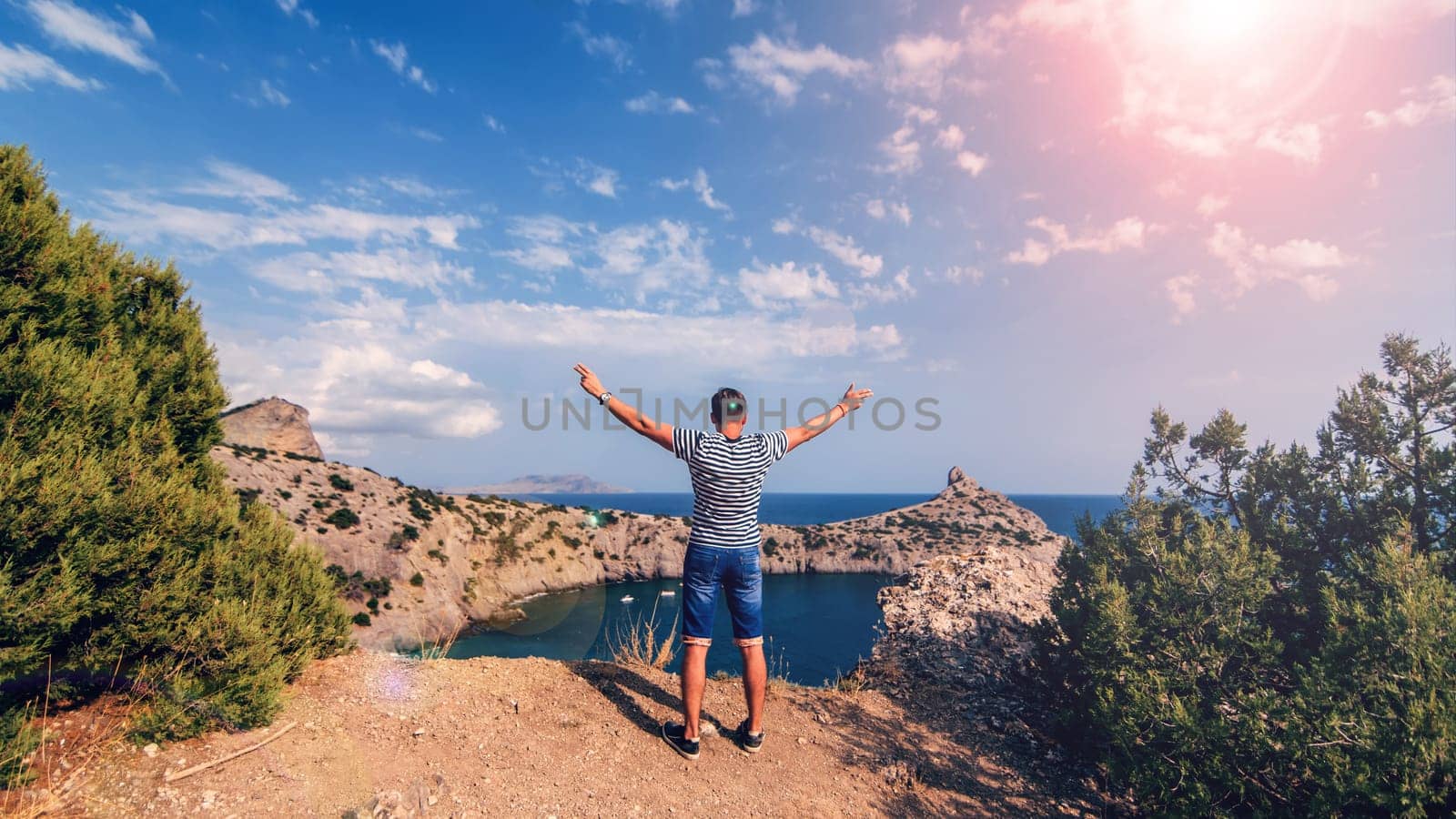 man traveler backs on top of mountains with his hands up against the sea and Sunny sky in summer. The concept of active lifestyle, success and achievements and freedom