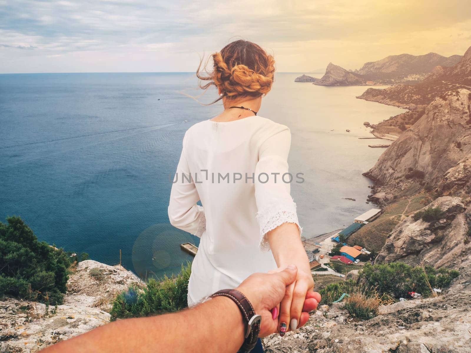 Follow me. Girl holds and leads her boyfriend by the hand in the mountains by the sea in the summer journey. Couple together resting on a Sunny day