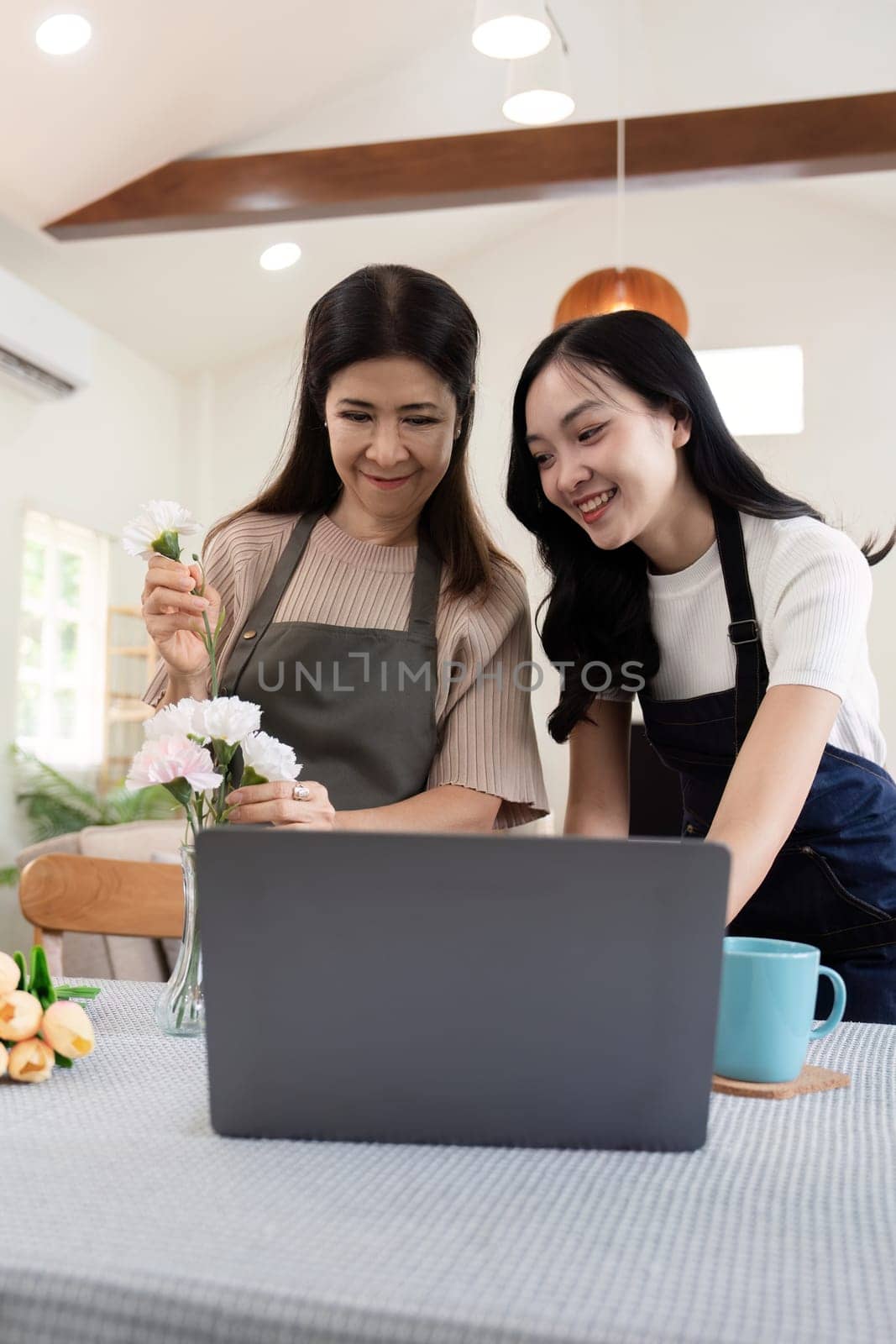 Happy mother and daughter arranging flower in vase at table in house do activities together on Mother's day.