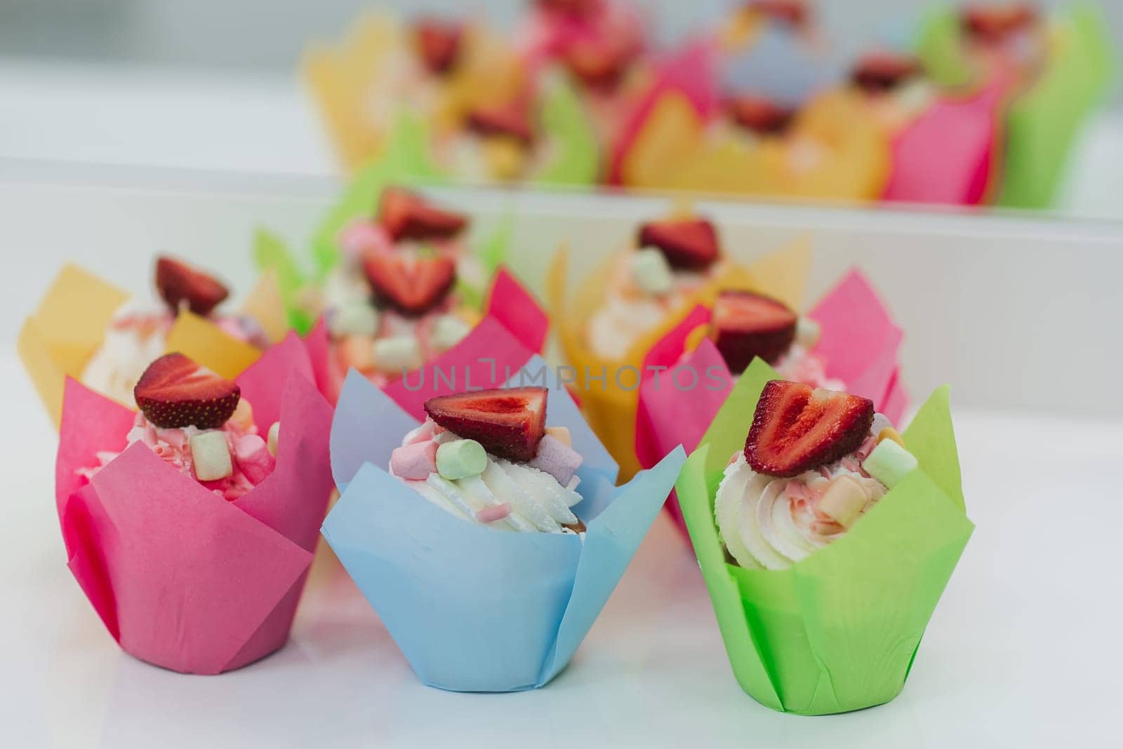 sweet multicolored cupcakes with fresh strawberries and white cream for the holiday close-up