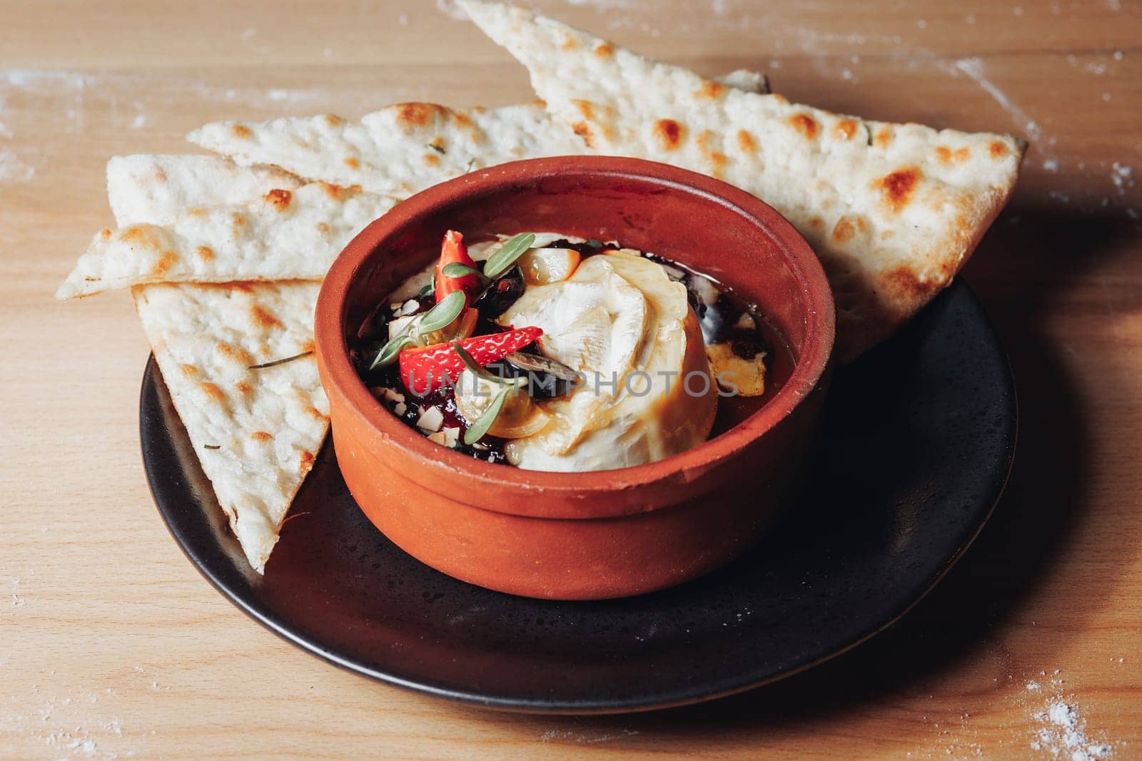 A tantalizing bowl of dip accompanied by fluffy pita bread, placed on a wooden table in a warm ambiance setting.