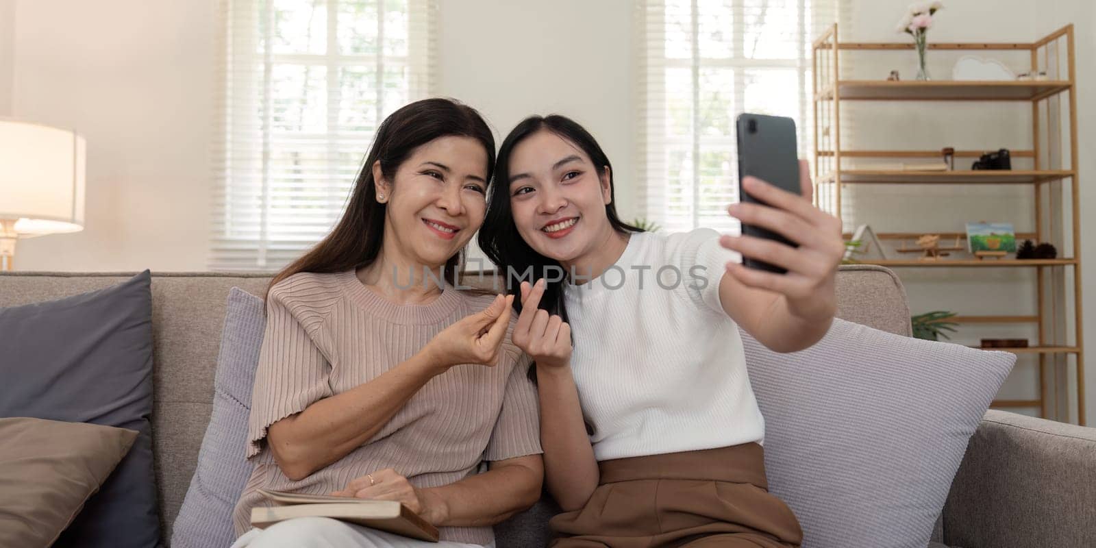 Daughter adult taking selfie using mobile phone with senior mother at home. Happy mother's day by nateemee