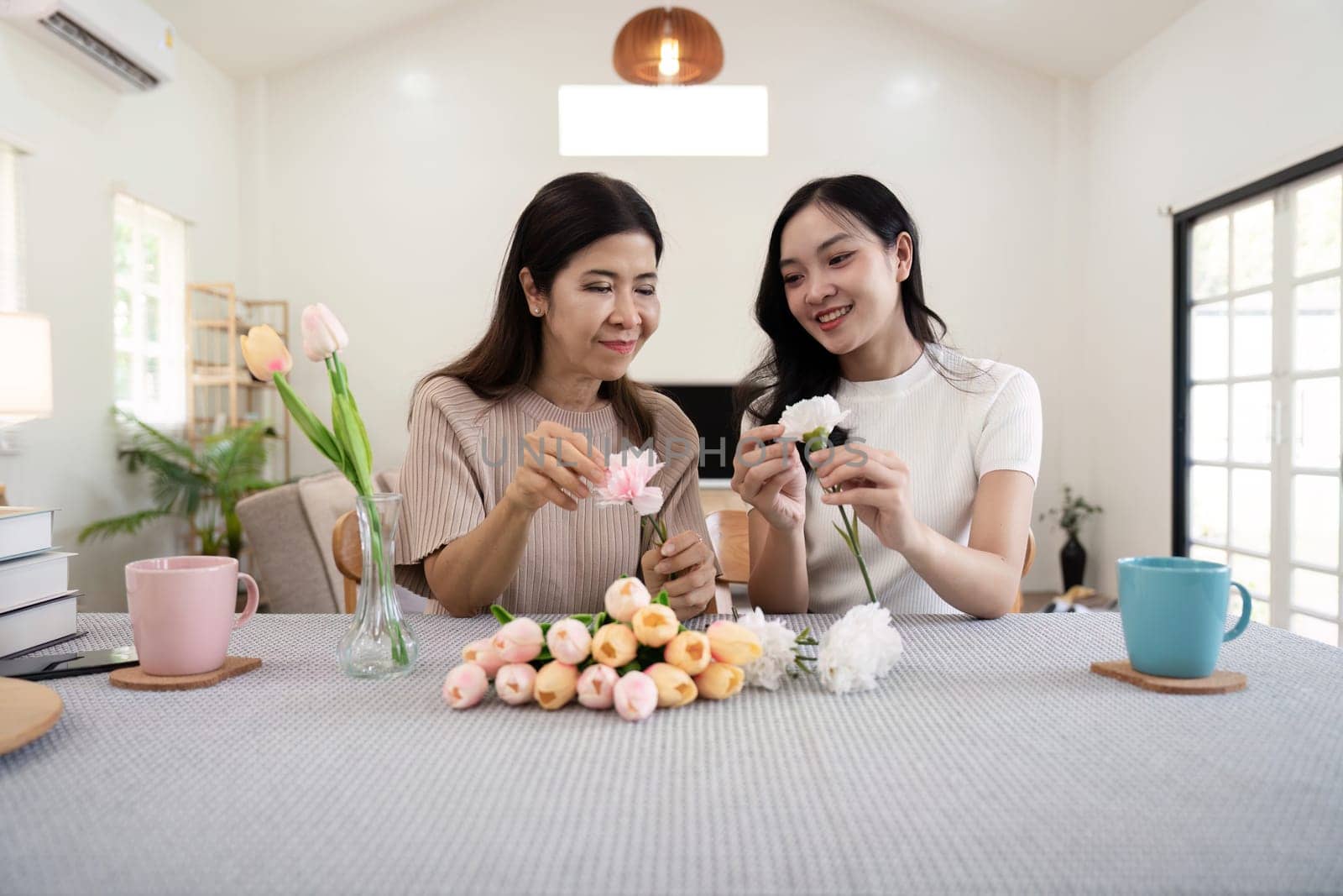 Happy mother and daughter arranging flower in vase at table in house do activities together on Mother's day.