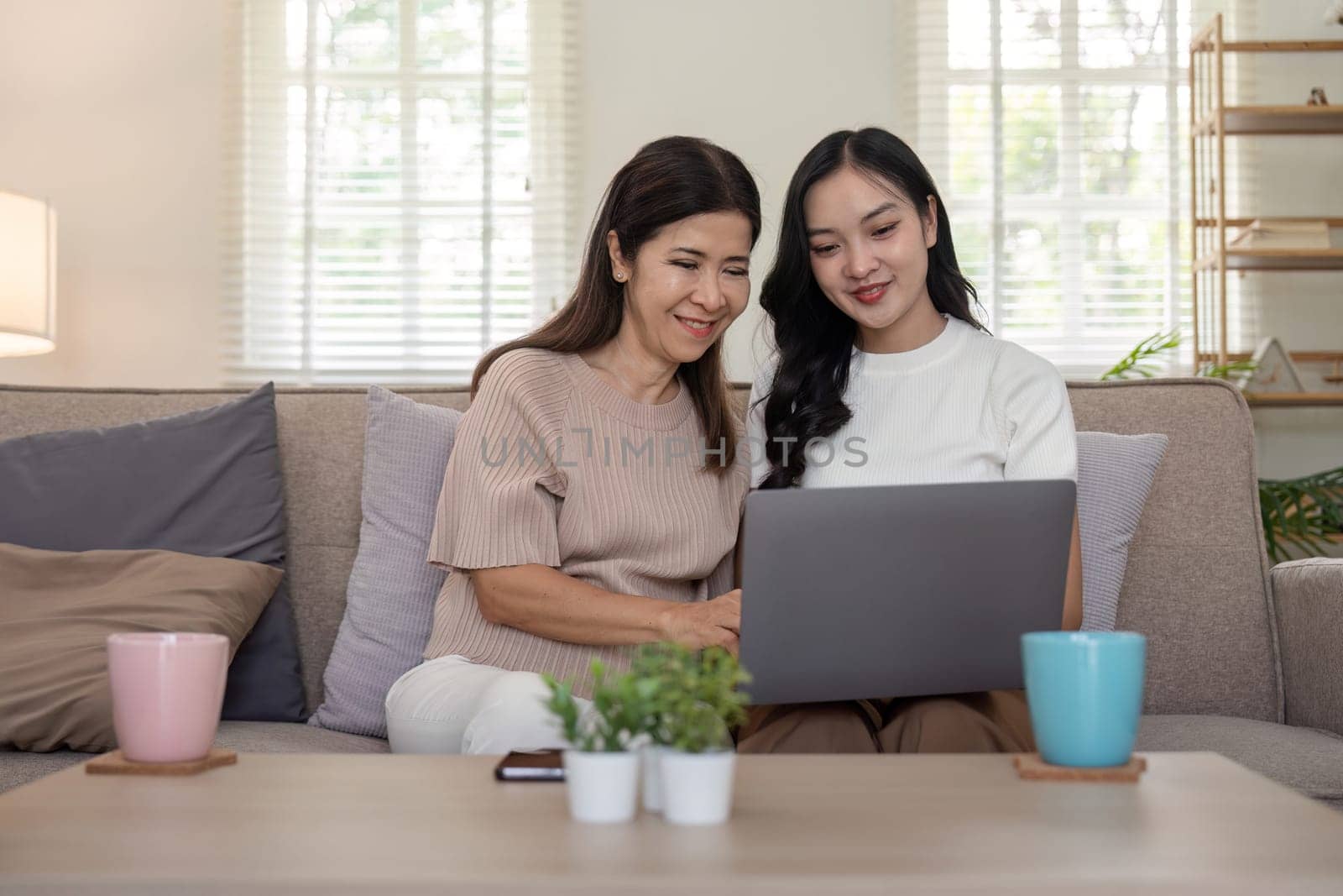 Happy mother and adult daughter use laptop having fun, sitting on couch at home, smiling woman embracing older mum, spending leisure time together. for Happy mother's day by nateemee