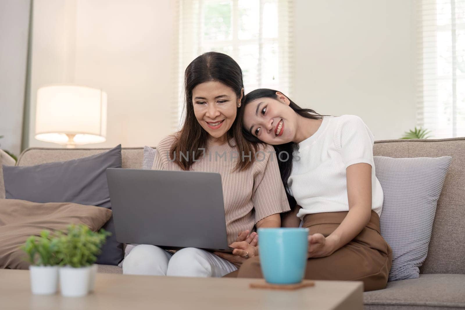 Happy mother and adult daughter use laptop having fun, sitting on couch at home, smiling woman embracing older mum, spending leisure time together. for Happy mother's day.