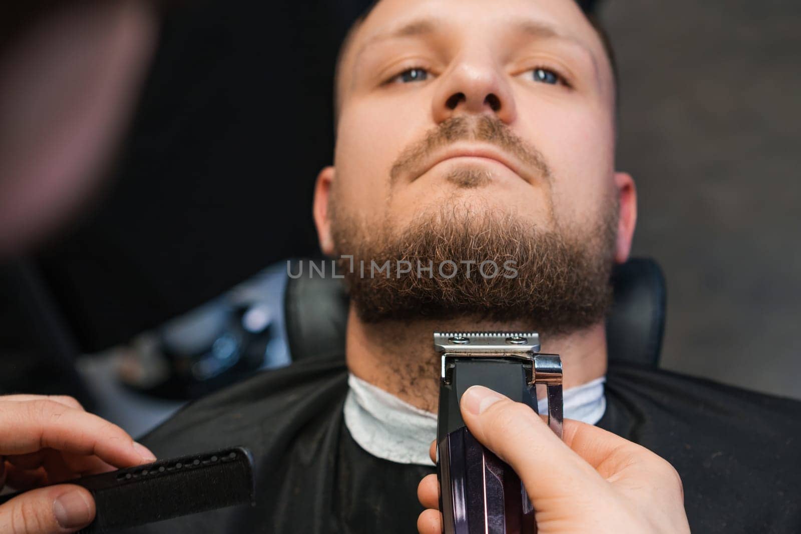 Master cuts client beard with trimmer in barbershop by vladimka