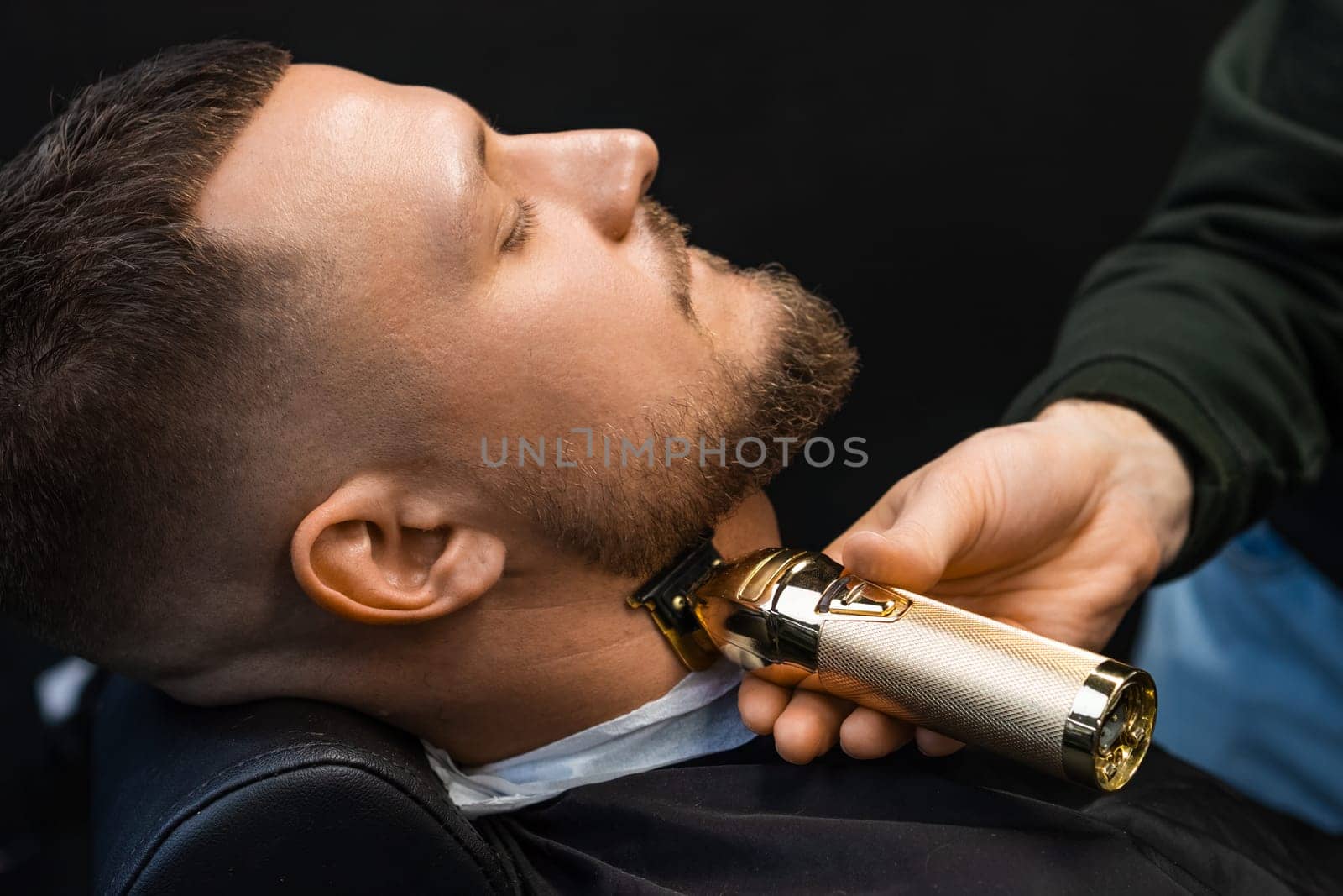 The barber uses an automatic trimmer to cut the client's beard at the barbershop. by vladimka