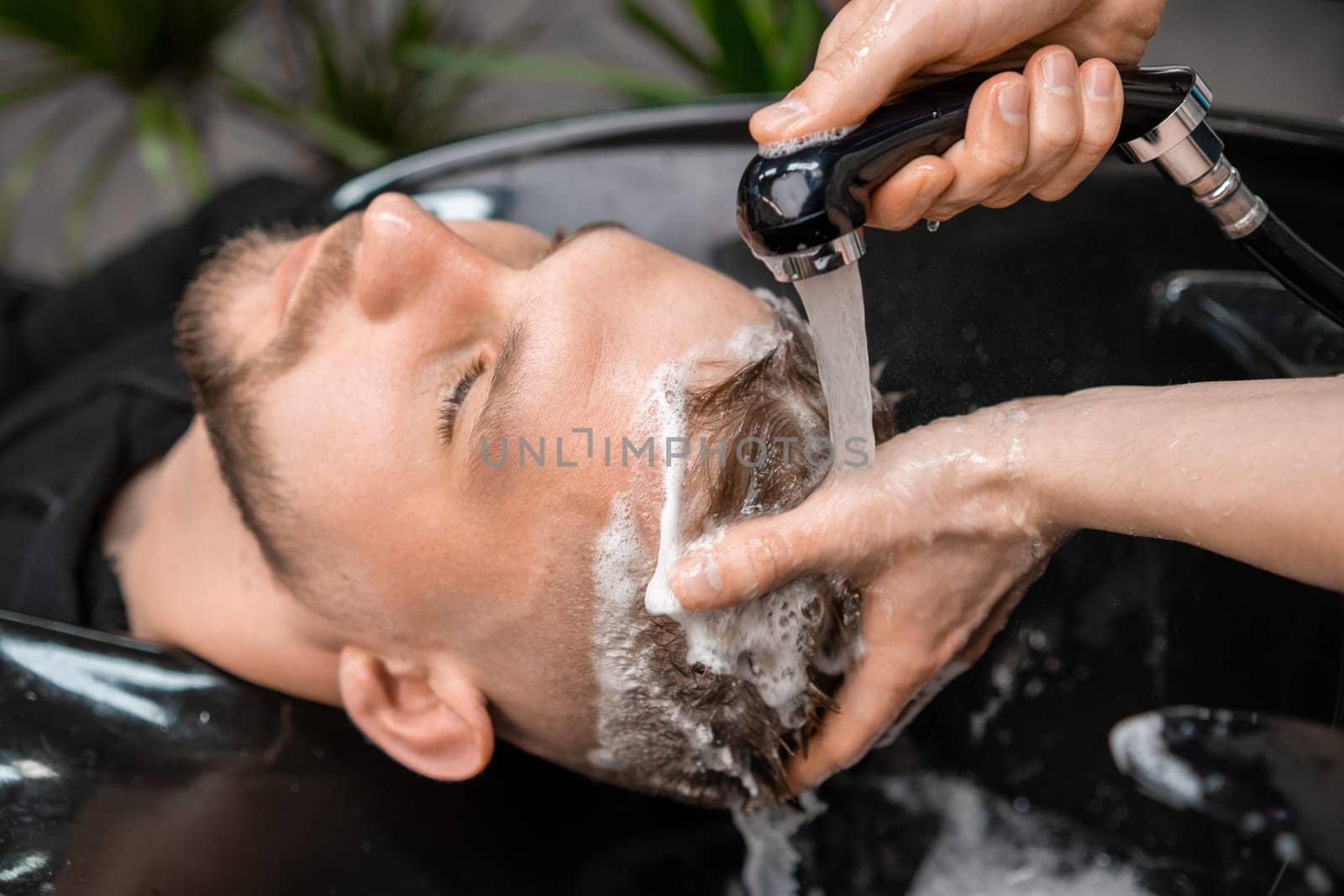 Skilled hairstylist tenderly rinses a clients hair from shampoo with warm water by vladimka
