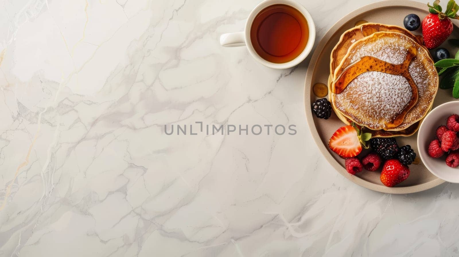 A delectable breakfast setup featuring pancakes topped with syrup and berries beside a cup of tea on a marbled surface. Banner with copy space.