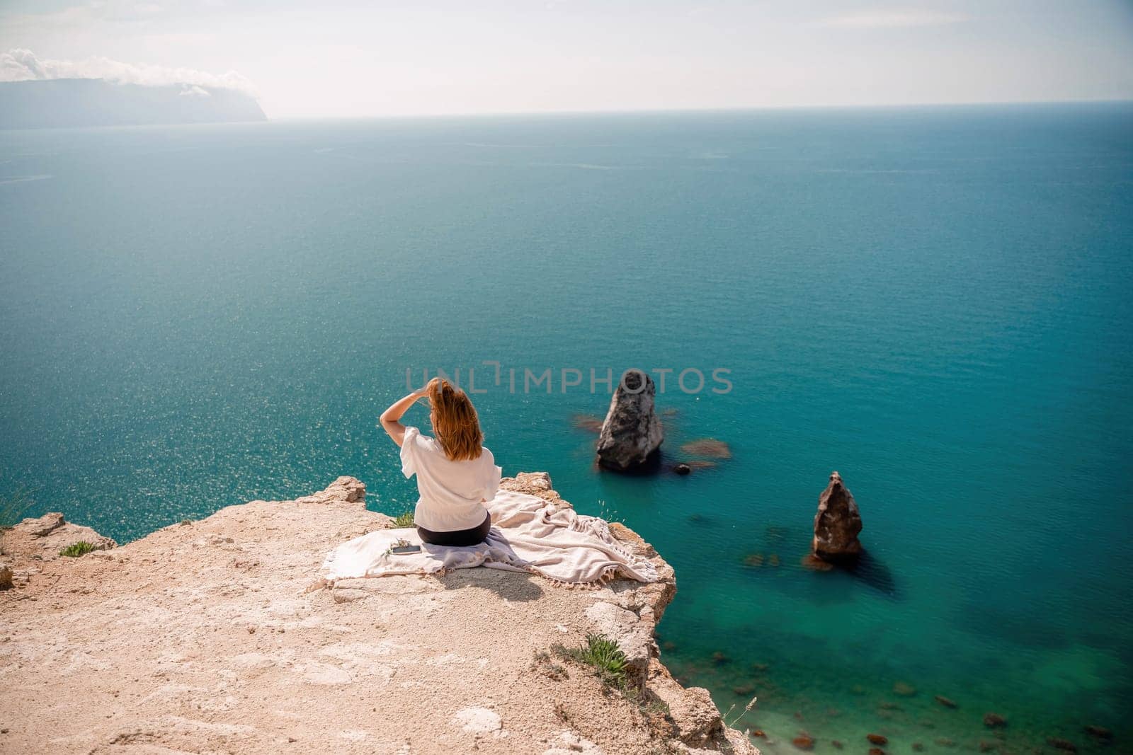 A woman is sitting on a rock overlooking the ocean. She is pointing to the water. The scene is peaceful and serene, with the woman enjoying the view and the calming sound of the waves