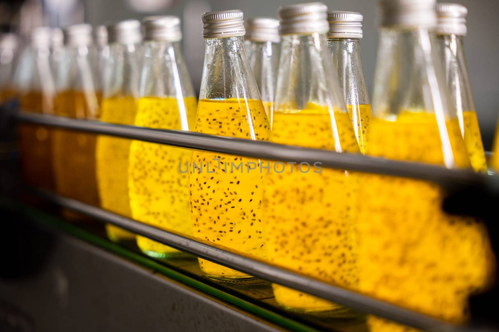 Basil or chia seed beverages with pomegranate undergo quality filling into transparent bottles on an automated conveyor belt in the beverage factory. Clean manufacturing ensures a healthy product.