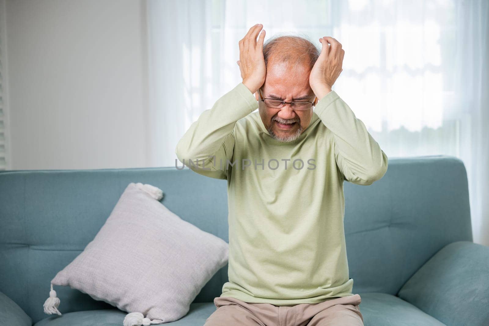 Sad Asian senior man sitting on sofa feeling hurt and lonely by Sorapop