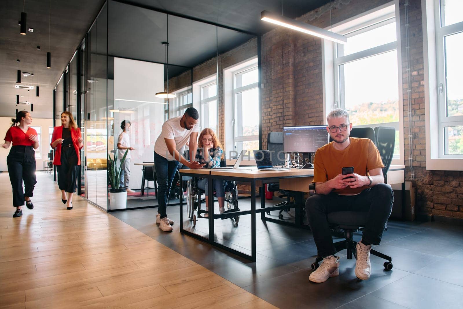 A diverse group of business professionals collaborates in a modern startup coworking center, utilizing a mix of paper-based and technological tools such as mobile phones and computers to collectively.
