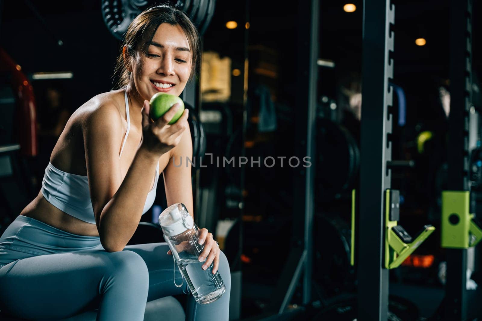 Asian woman holding a green apple in a fitness gym by Sorapop