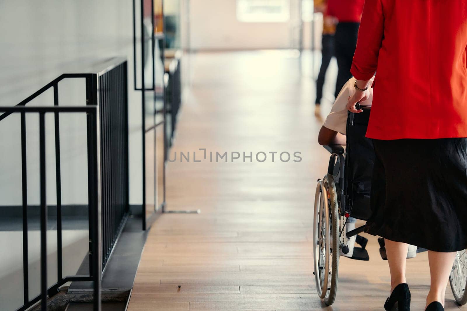 A businesswoman assists her colleague in a wheelchair as they navigate the sleek hallways of a modern startup office, embodying inclusivity and teamwork.