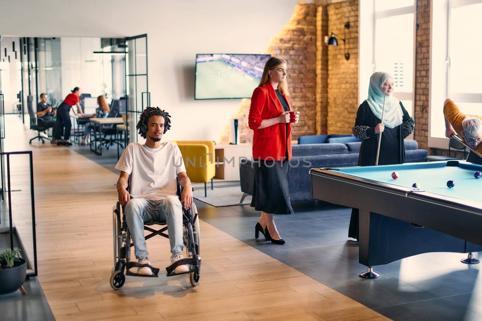 An African-American young entrepreneur in a wheelchair is surrounded by his business colleagues in a modern office setting, embodying diversity and collaboration in the workplace by dotshock