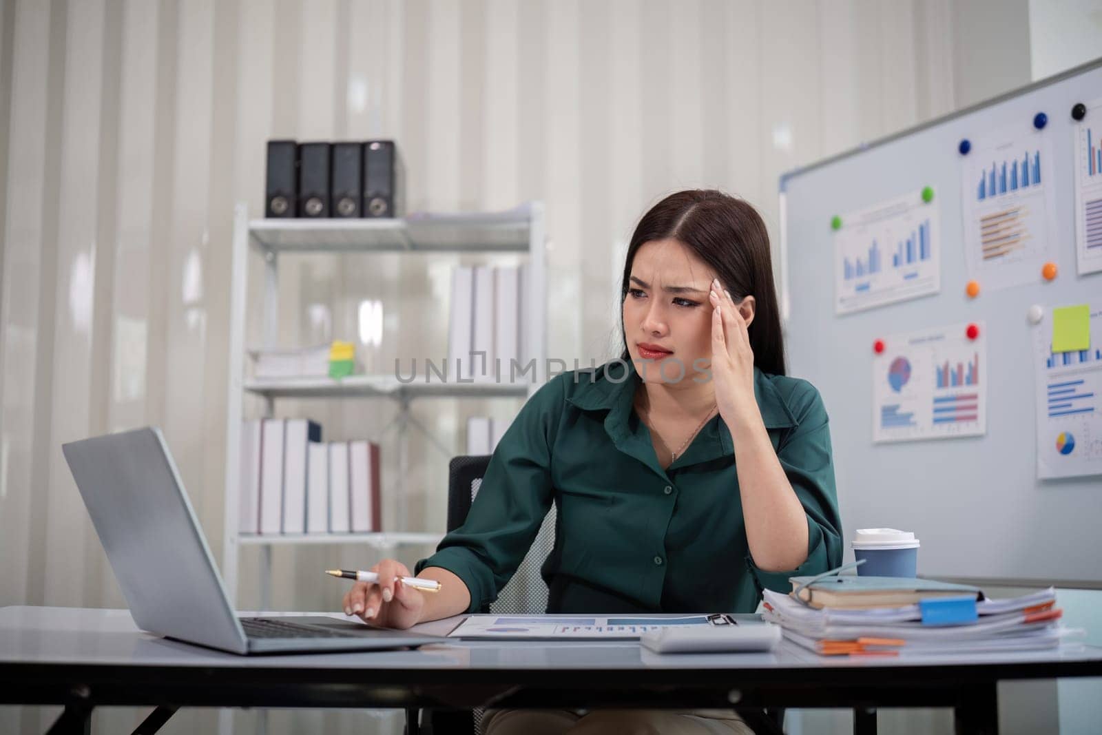 Stressed overwhelmed businesswoman working with computer laptop while having headache in the office.