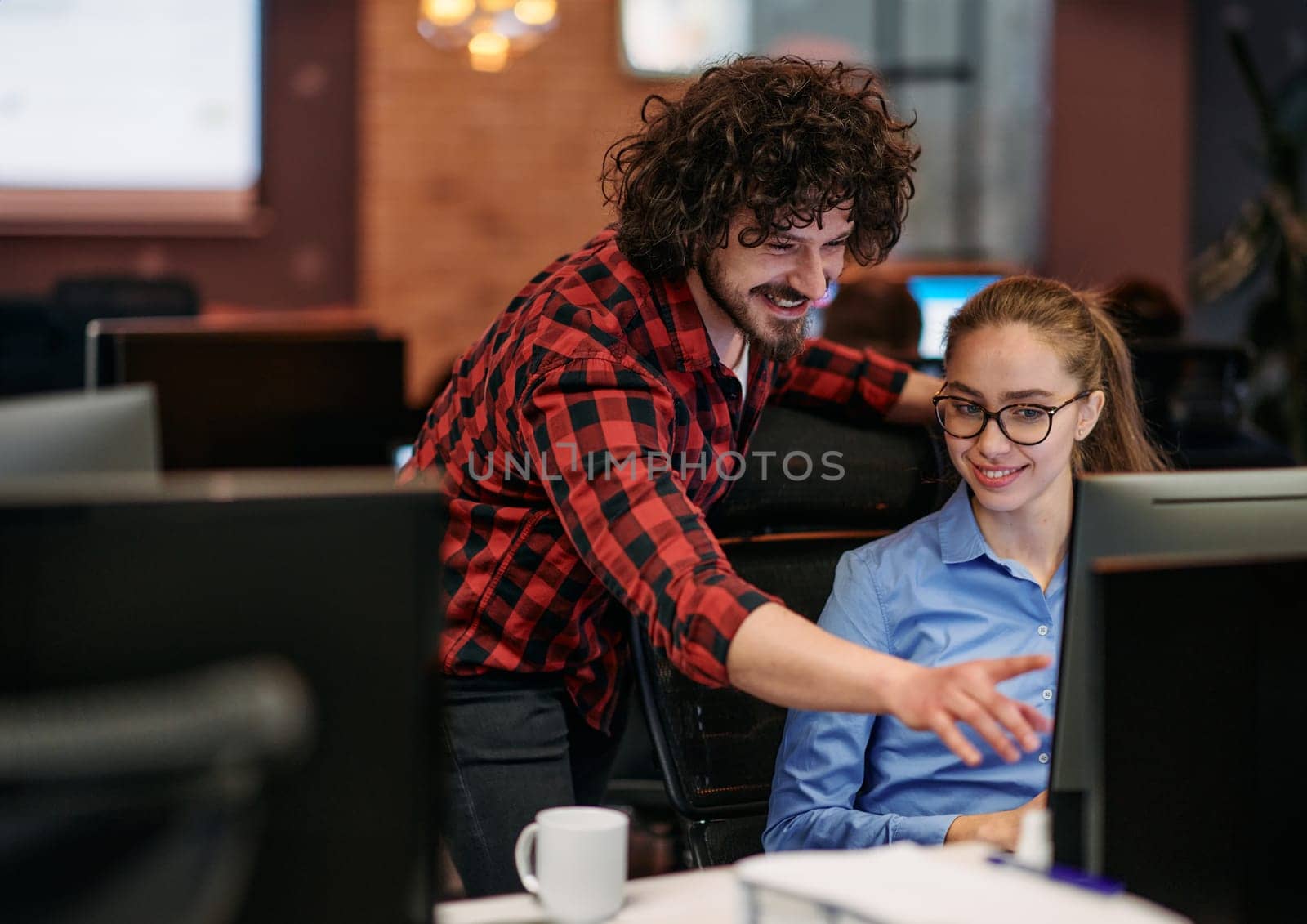 Business colleagues, a man and a woman, engage in discussing business strategies while attentively gazing at a computer monitor, epitomizing collaboration and innovation.
