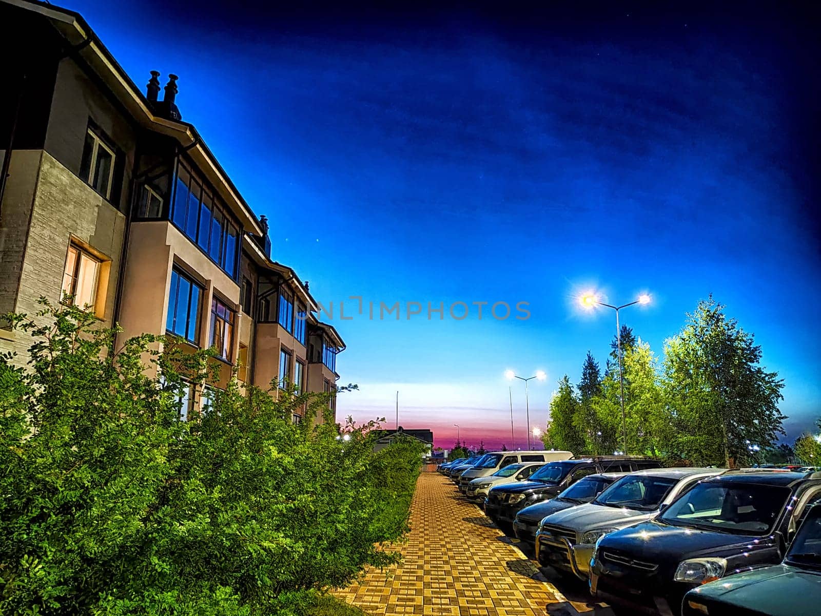 Night, village, houses and cars in the parking lot. Photography is like painting. Serene Village Nightfall With Parked Cars and Illuminated Homes