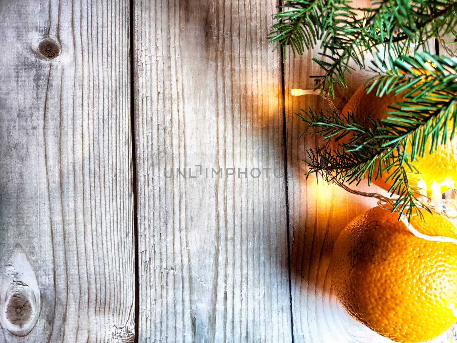 Festive decoration with bouquet and branches of spruce, bright glowing garlands, oranges on wooden background. Decor for Christmas and New Year. Abstract texture, frame, place for text, copy space by keleny
