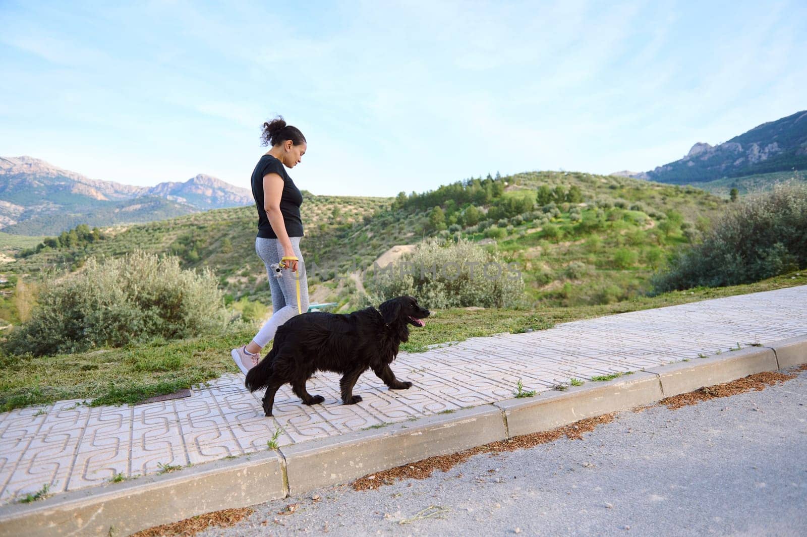 Full length shot of a woman in active wear, walking her dog on the mountains nature. Domestic animals, pets and people concept by artgf