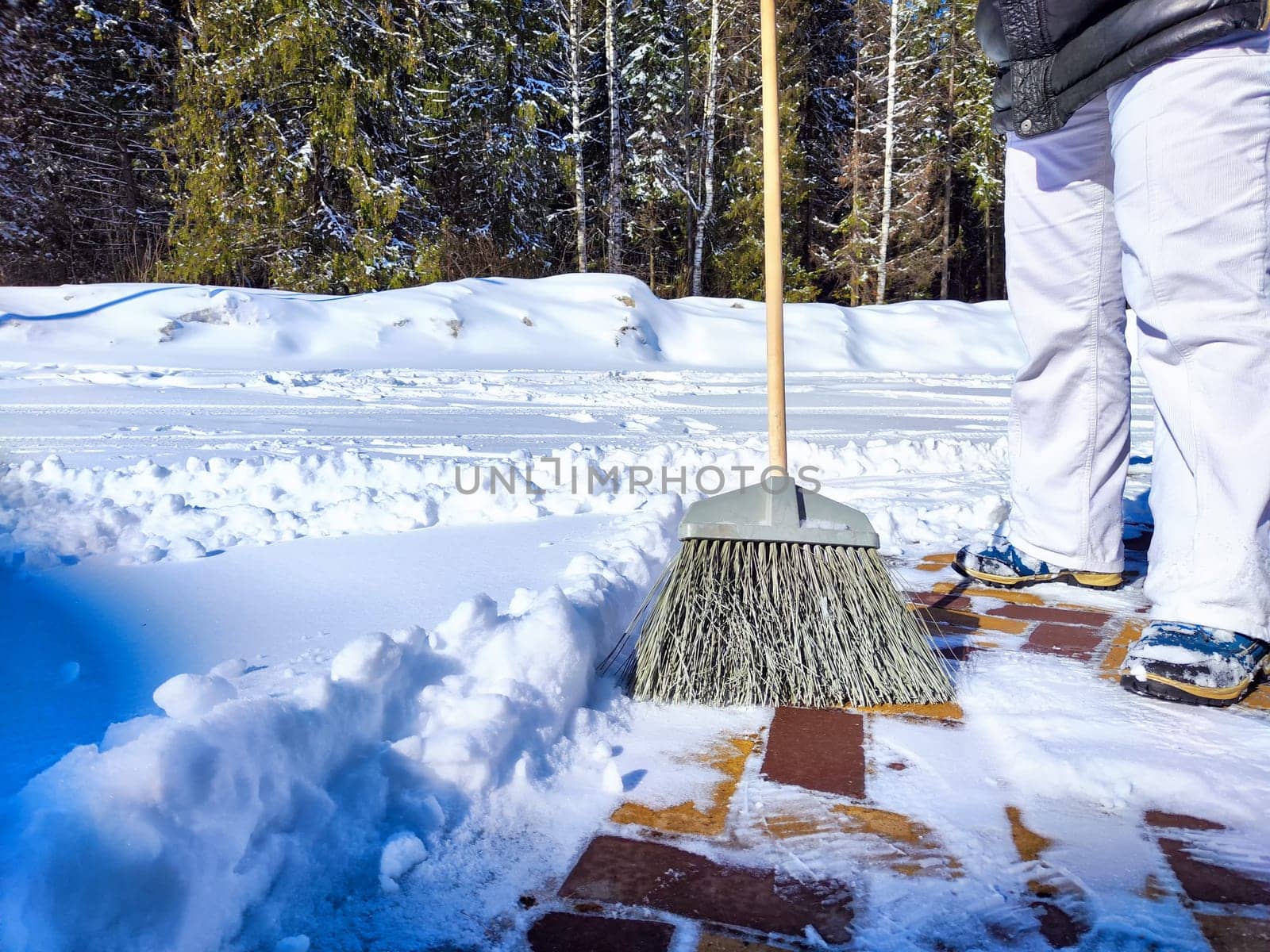 Clearing Snow From Sunny Yard With Broom. Person sweeps fresh snow off the brick path in front of house