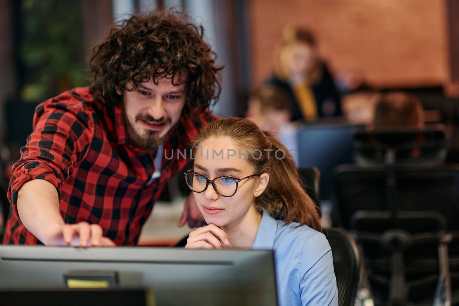 Business colleagues, a man and a woman, engage in discussing business strategies while attentively gazing at a computer monitor, epitomizing collaboration and innovation by dotshock