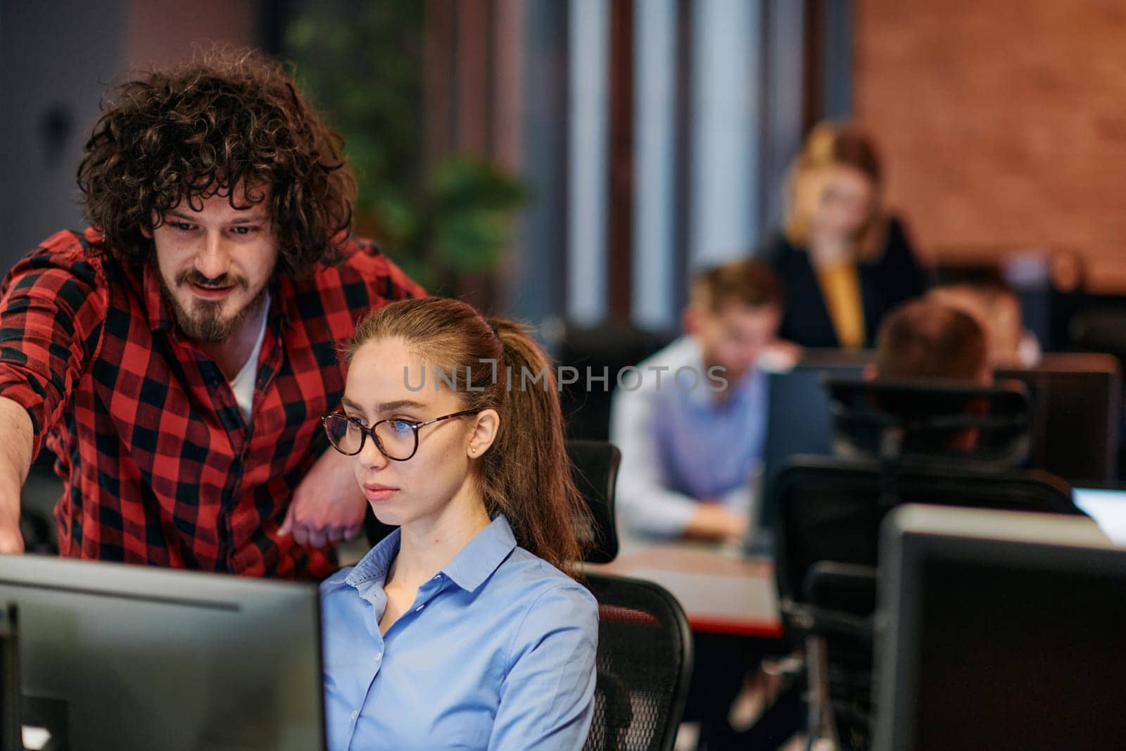 Business colleagues, a man and a woman, engage in discussing business strategies while attentively gazing at a computer monitor, epitomizing collaboration and innovation by dotshock