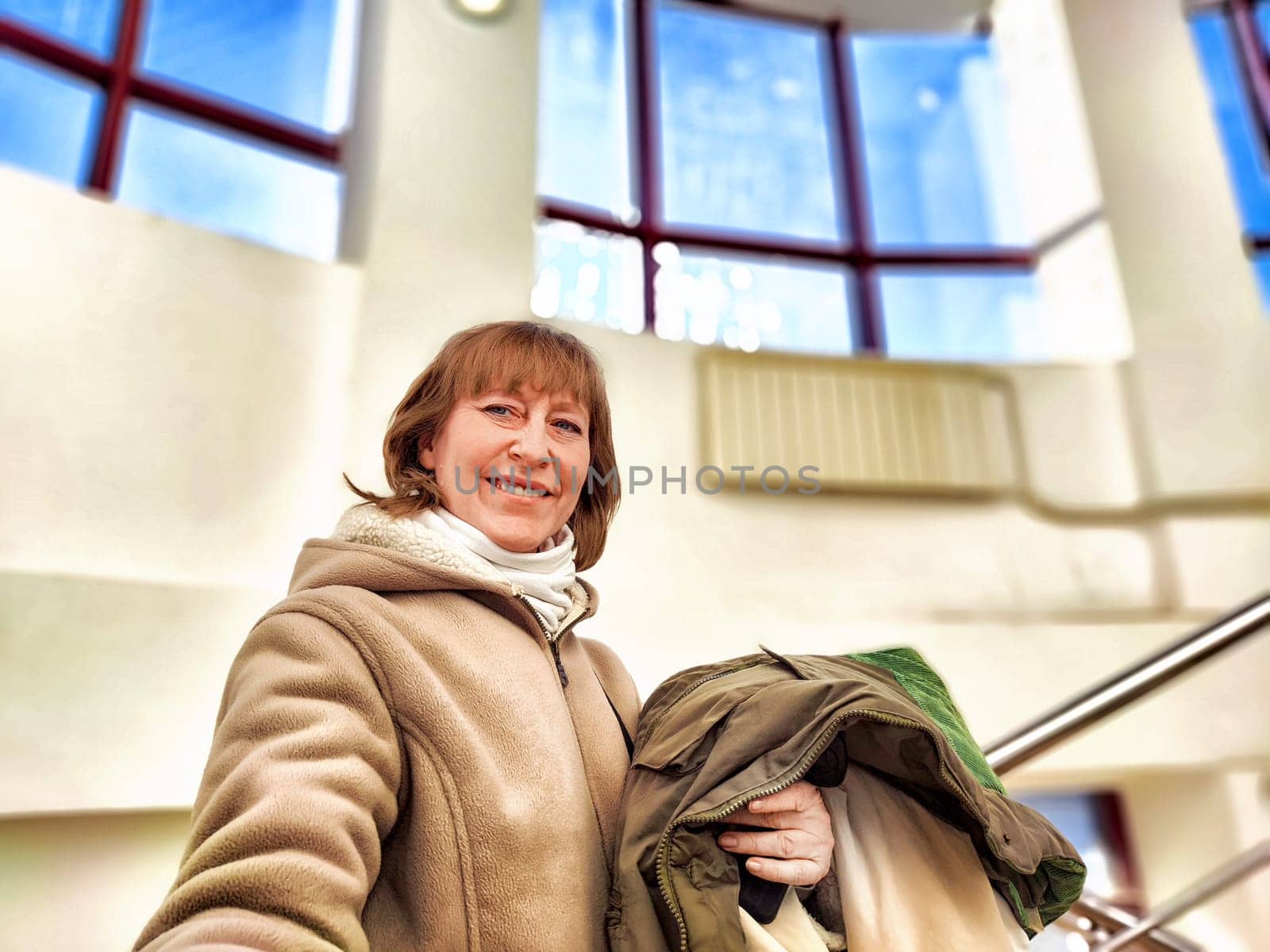 Middle-Aged Woman Shopping Second-Hand Clothes in Store, Smiling woman holding eco-friendly second-hand garments