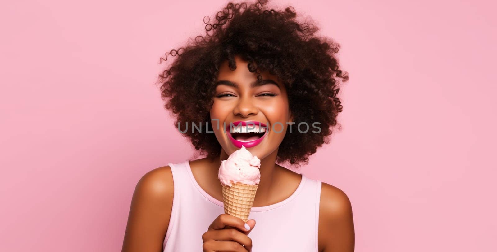 Summer portrait of happy cheerful young African woman eating ice cream cone on pink studio background