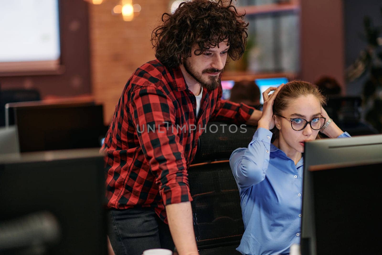 Business colleagues, a man and a woman, engage in discussing business strategies while attentively gazing at a computer monitor, epitomizing collaboration and innovation.