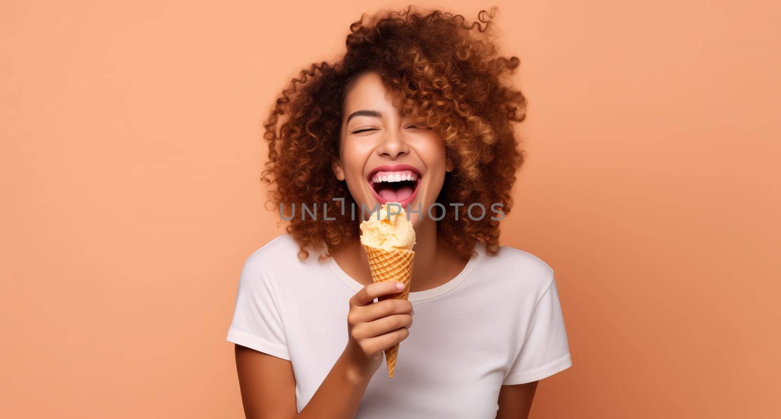 Summer portrait of happy cheerful smiling young woman eating ice cream cone, curly hair, on orange studio background