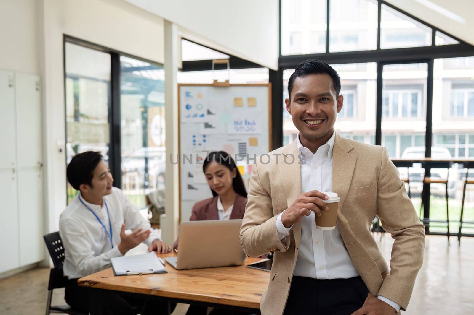 Smiling confident businessman looking at camera and standing in an office at team meeting. Portrait of confident businessman with colleagues in boardroom.